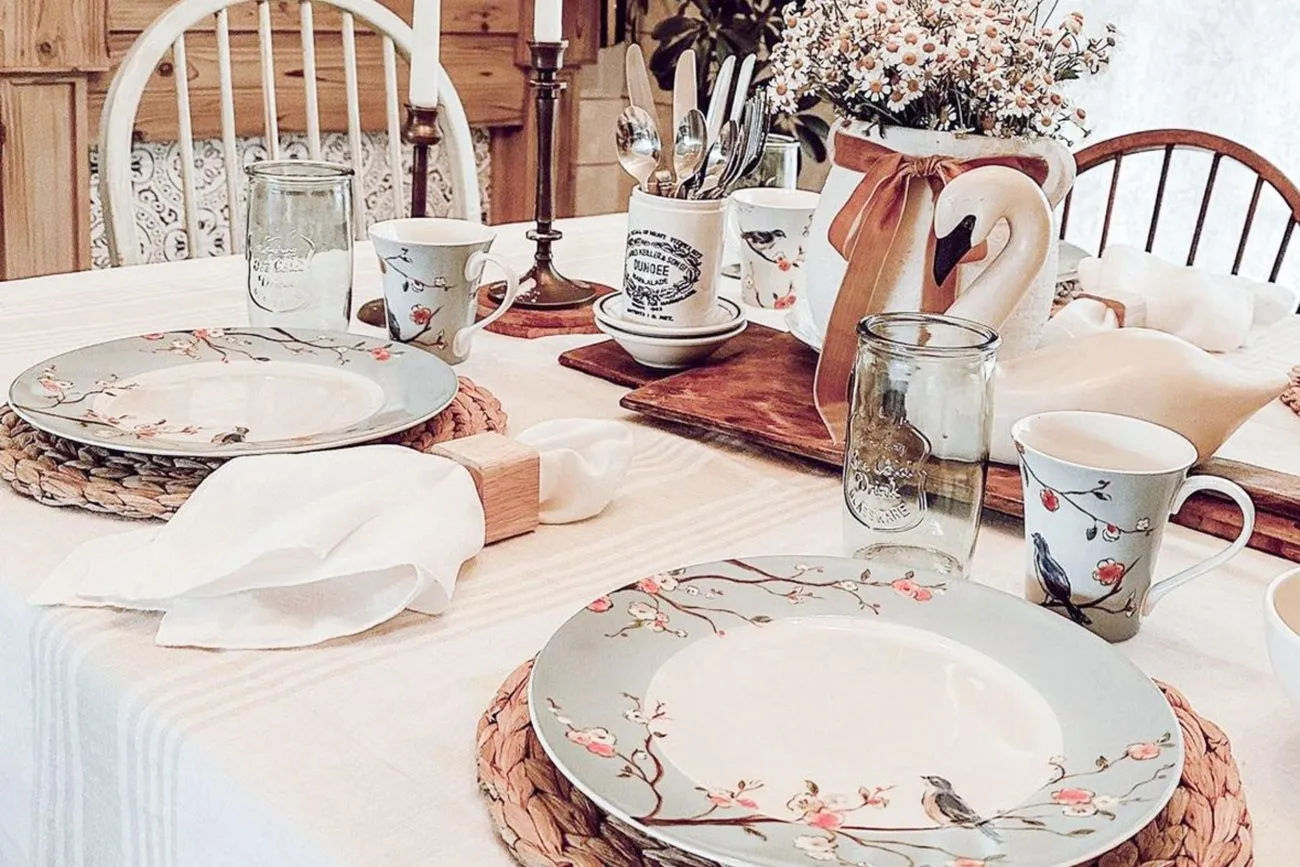 Mesa vestida con mantelería blanca, vajilla de flores y servilletas dobladas